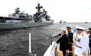 Putin standing at a fence on a dock looking at a battleship