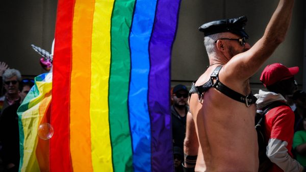 LGBT Pride flag held by a man wearing leather
