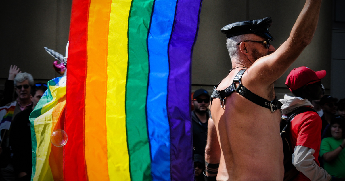 LGBT Pride flag held by a man wearing leather