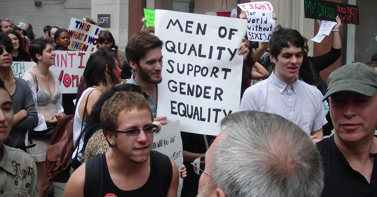 Male feminists protesting with a sign that reads "Men of quality support gender equality"