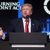 Donald Trump with his arms outstretched in front of a TPUSA background