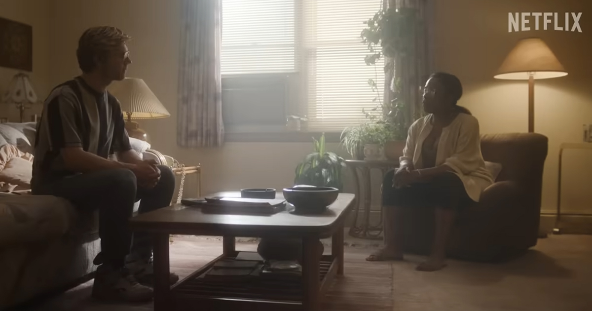 Still image from trailer depicting Dahmer and a black woman sitting in a livingroom