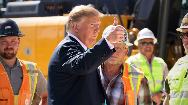 Donald Trump raises his fist while standing next to four men wearing high-vee vests