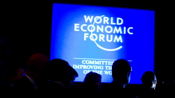Klaus Schwab and a World Economic Forum screen with attendees in the foreground