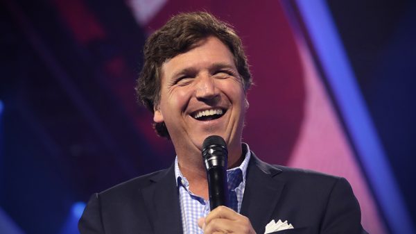 Tucker Carlson laughing while holding a microphone