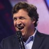 Tucker Carlson on a stage holding a microphone