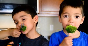 Two children eat broccoli with a fork