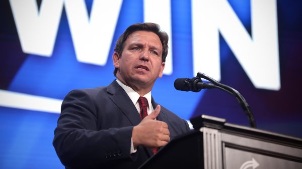 Ron DeSantis in front of a sign that says "win"