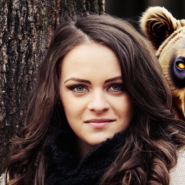 A woman standing next to a tree with an artificial bear behind her